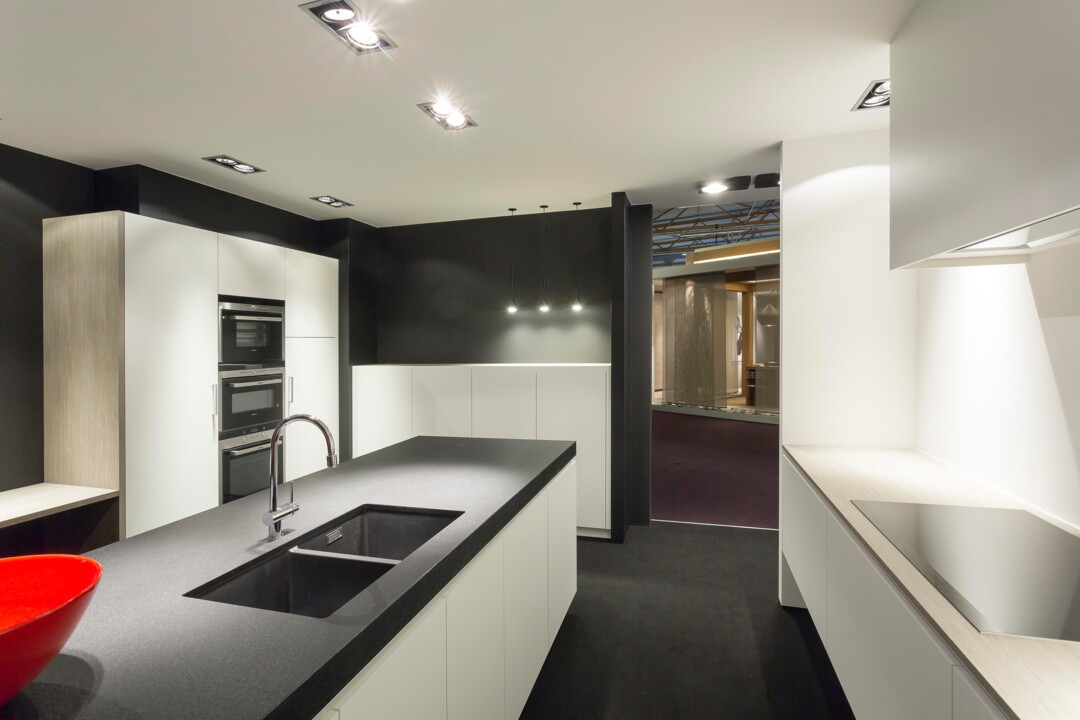 Deze mooie moderne design keuken werd op de bisbeurs tentoongesteld door Woonproject Aalter. De keuken is wit gelakt met een natuursteen werkblad